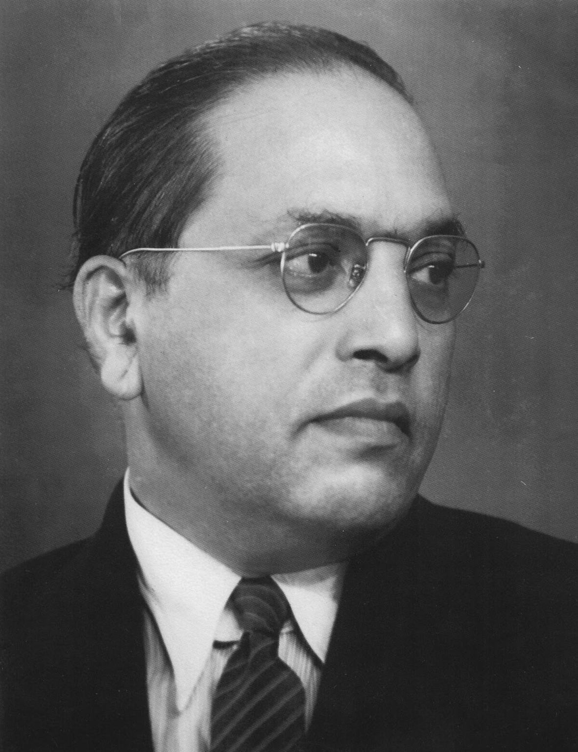 B. R. Ambedkar in a formal portrait photograph, showcasing his distinctive look with round glasses and suit