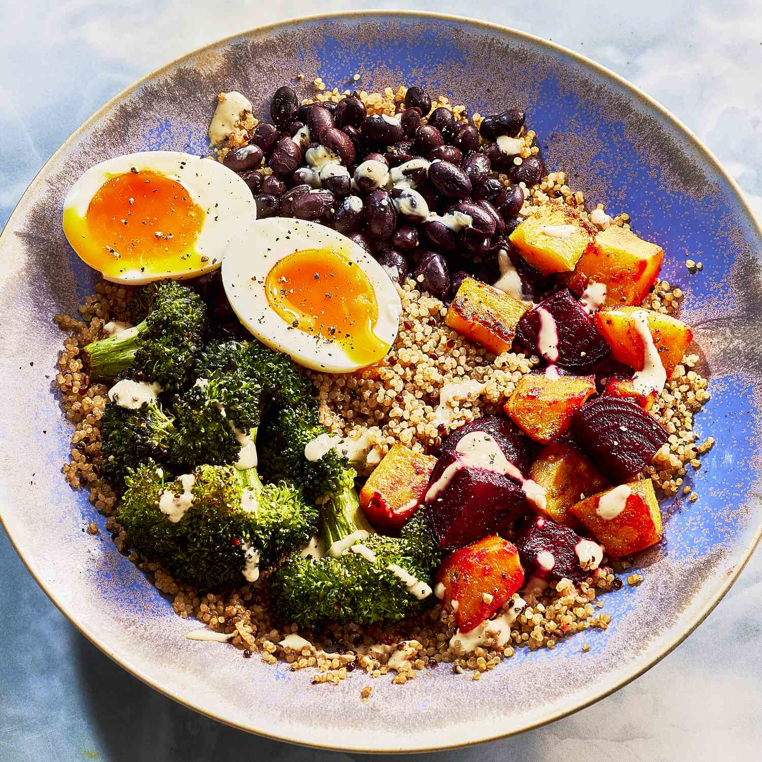 A healthy breakfast bowl featuring quinoa, soft-boiled eggs, black beans, broccoli, roasted root vegetables, and a light dressing, illustrating balanced nutrition