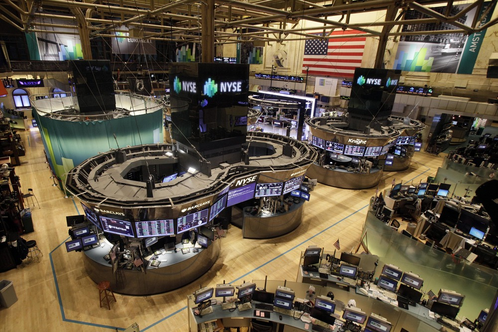 The New York Stock Exchange trading floor featuring multiple trading desks and large electronic displays showing market data