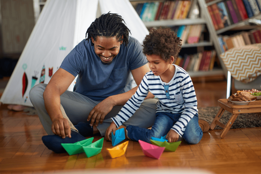 An adult and child engaged in floor play with colorful paper boats, illustrating a key aspect of DIR/Floortime therapy for autism.