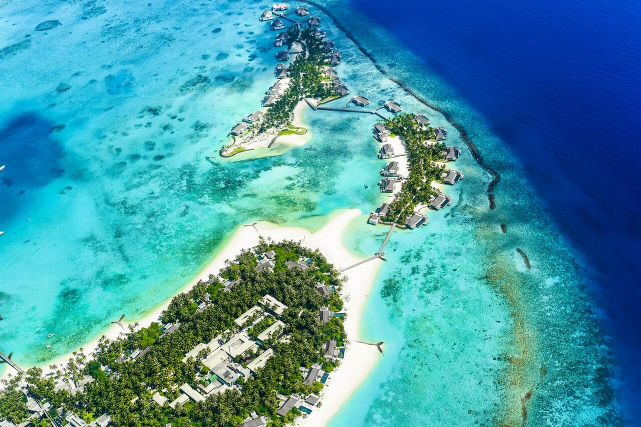 Aerial view of interconnected islands in the Maldives showing lush vegetation, water villas, and coral lagoon waters