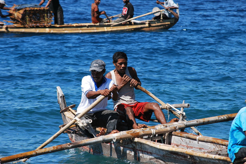 Two men rowing a traditional wooden fishing boat on the clear waters of the Maldives, illustrating local island fishing practices