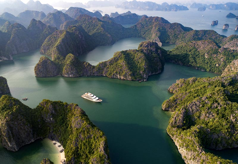 Aerial view of Halong Bay's limestone karsts and emerald waters with a boat cruising through the bay