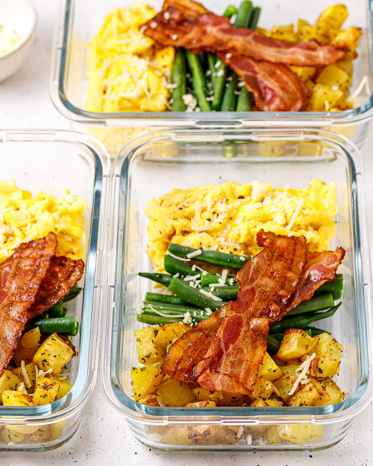 Meal prep containers with balanced breakfast of eggs, green beans, potatoes, and bacon