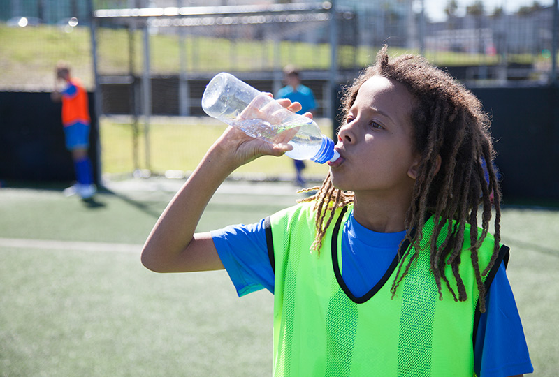 Teenage athlete staying hydrated during soccer practice by drinking water from a bottle