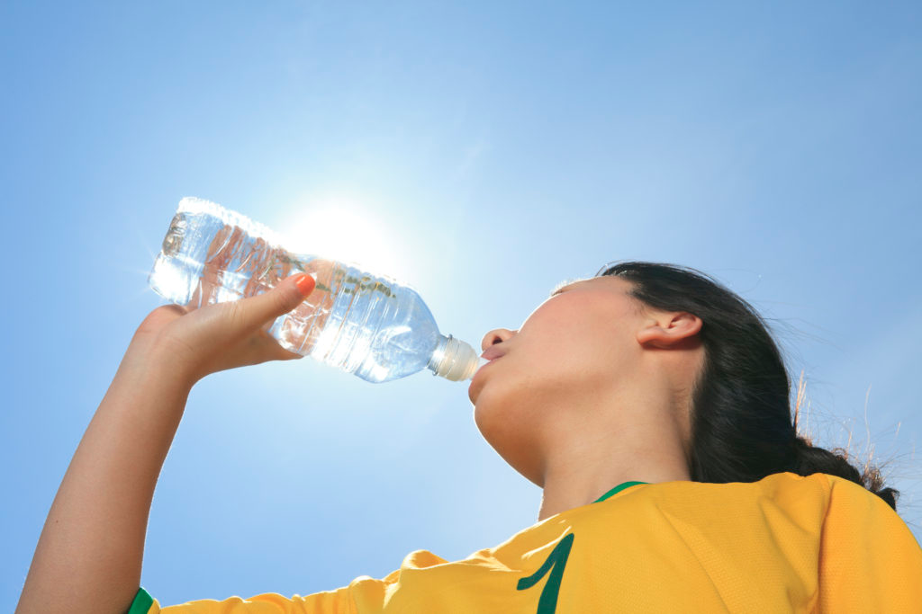 A teenage athlete drinks water to stay hydrated during sports training
