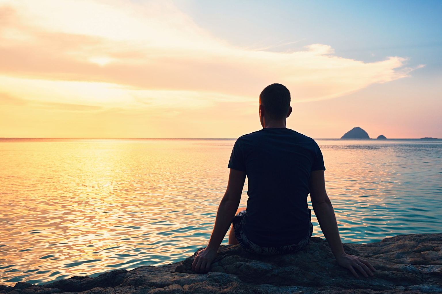 A person sits contemplatively by the sea at sunset, symbolizing peace and acceptance of uncertainty.
