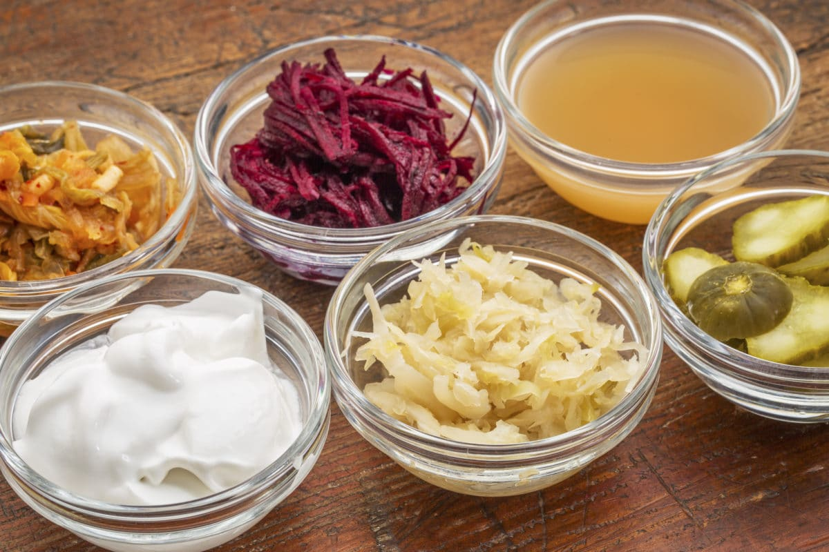 Various probiotic fermented foods including kimchi, beetroot, sauerkraut, yogurt, and pickles in glass bowls