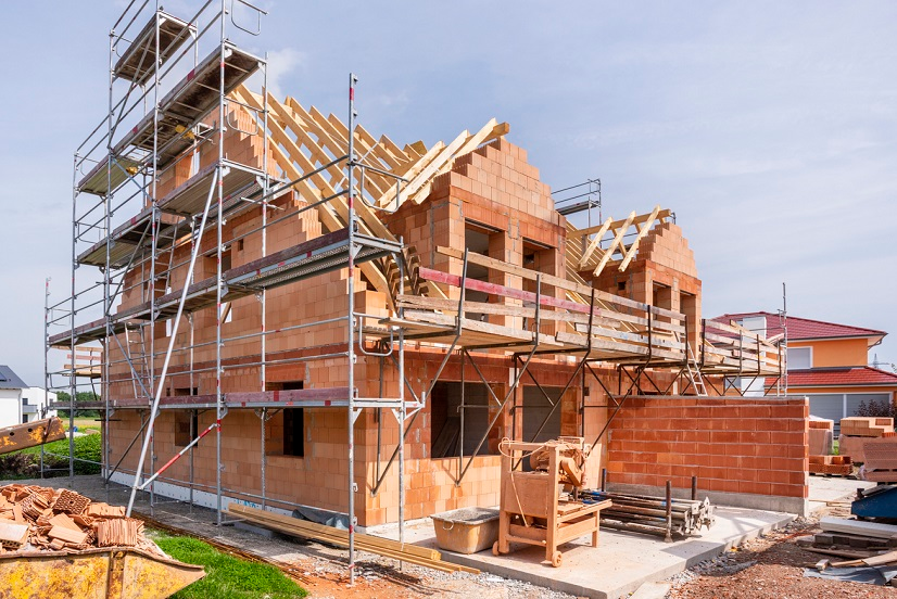A Single-Family House Under Construction Showcasing Brickwork And Roofing Framework With Scaffolding In Place