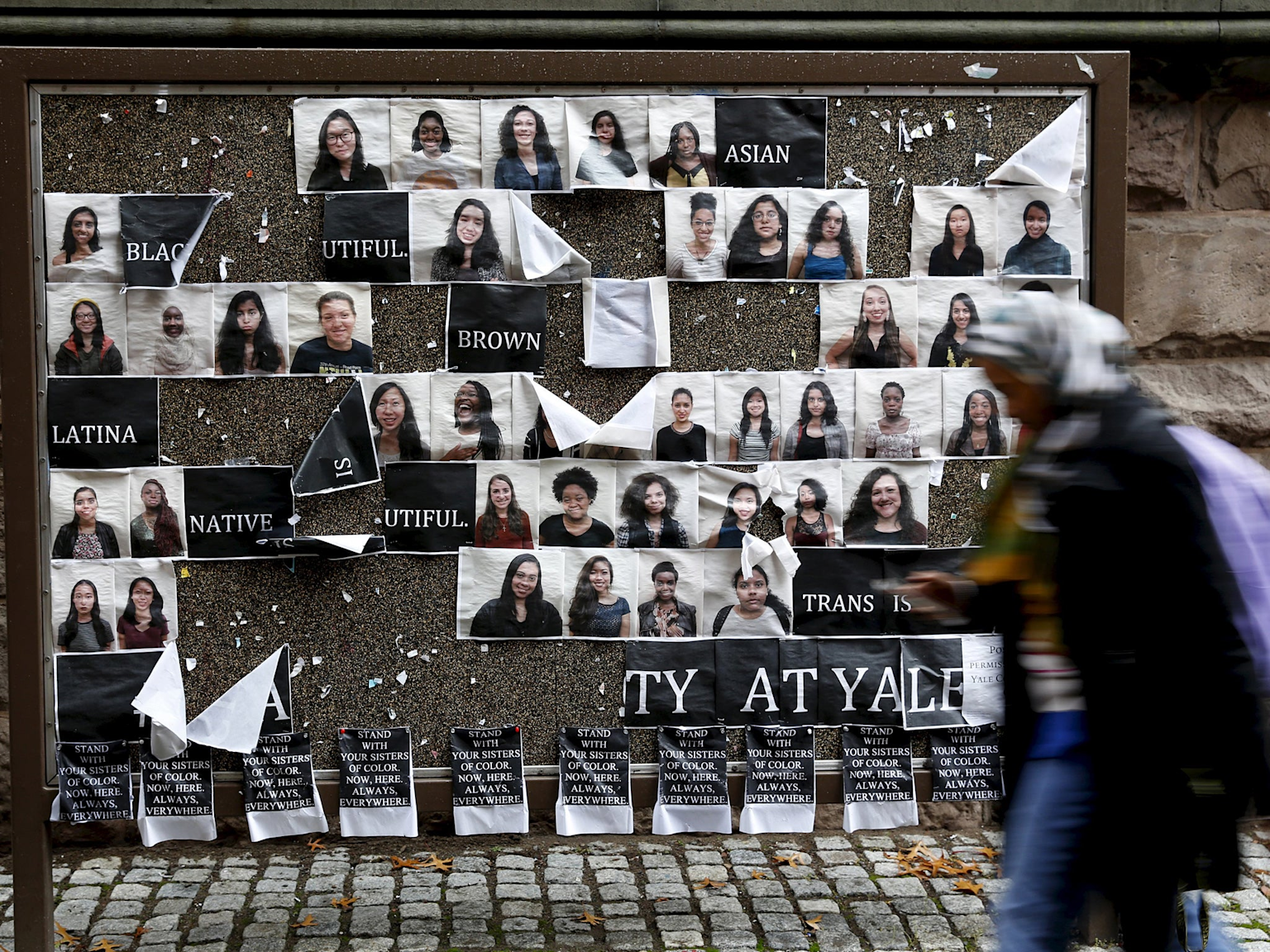 A university campus bulletin board displaying photos and labels related to racial and identity categories during a social justice protest or activism event
