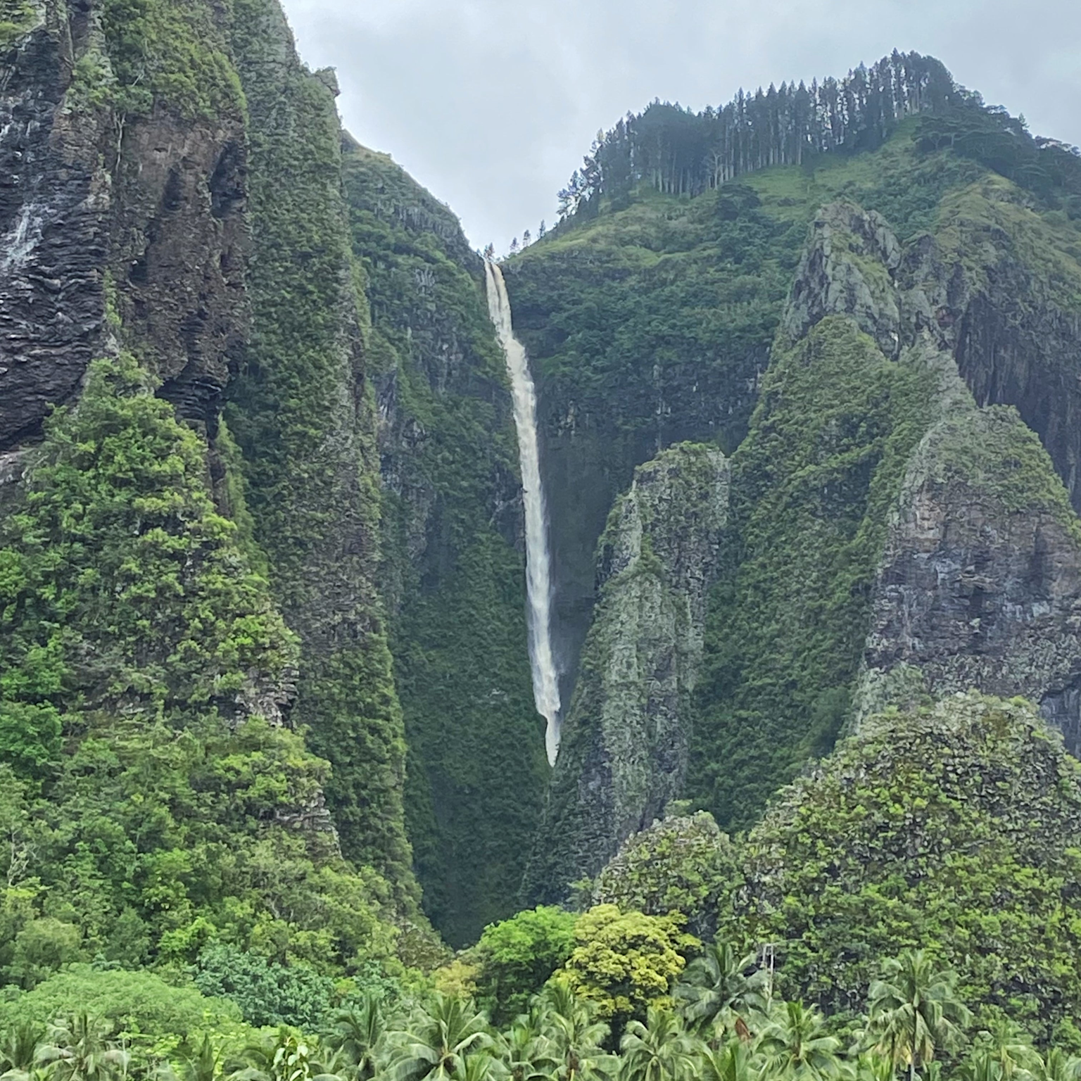 Dramatic cliffs and a cascading waterfall in Nuku Hiva, Marquesas Islands, showcasing the island's lush and adventurous landscape