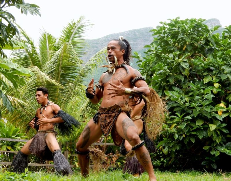 Traditional Polynesian dancers performing a vibrant cultural dance amidst tropical greenery and mountainous backdrop in the Marquesas Islands