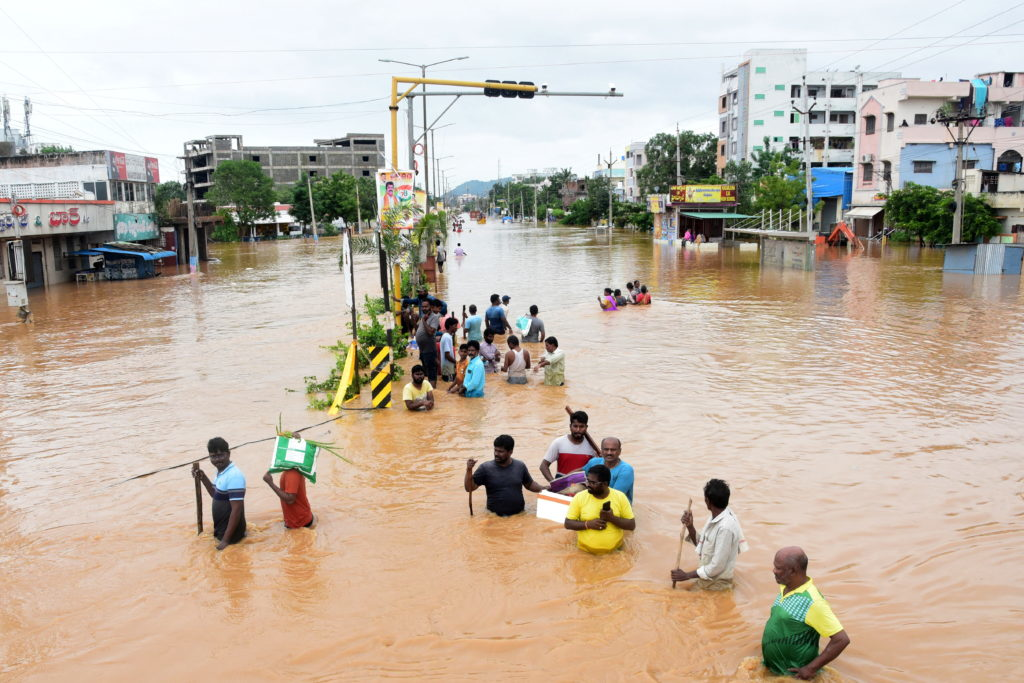 Severe urban flooding with residents wading through waist-deep muddy water during monsoon floods causing disruptions including school closures