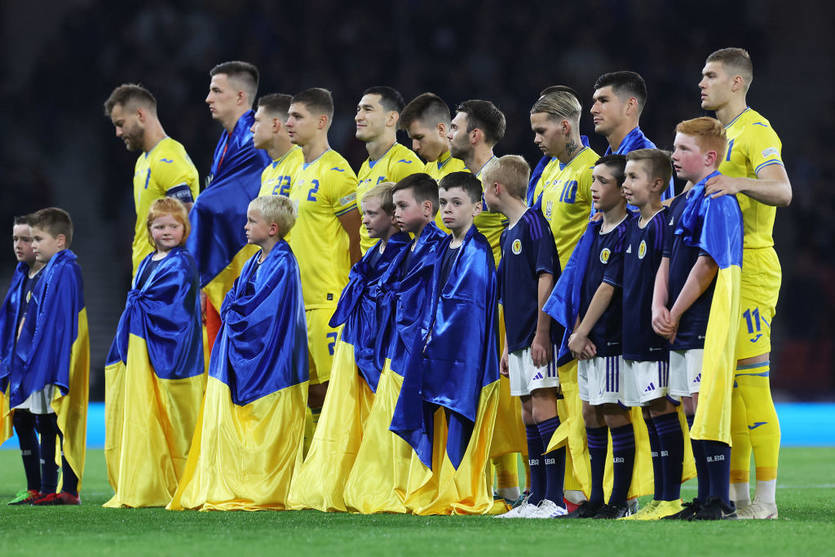 Ukrainian national football team standing with children wrapped in Ukrainian flags during a pre-match ceremony