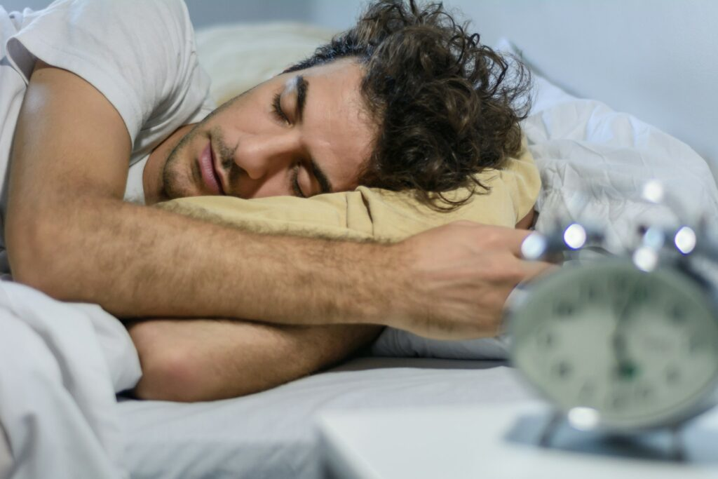 Person reaching to turn off an alarm clock, illustrating the importance of sleep in recovery and injury prevention for athletes