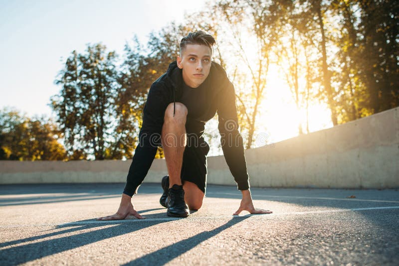 An athlete in a starting sprint position during an evening training session outdoors, exemplifying training timed to the body's natural rhythms