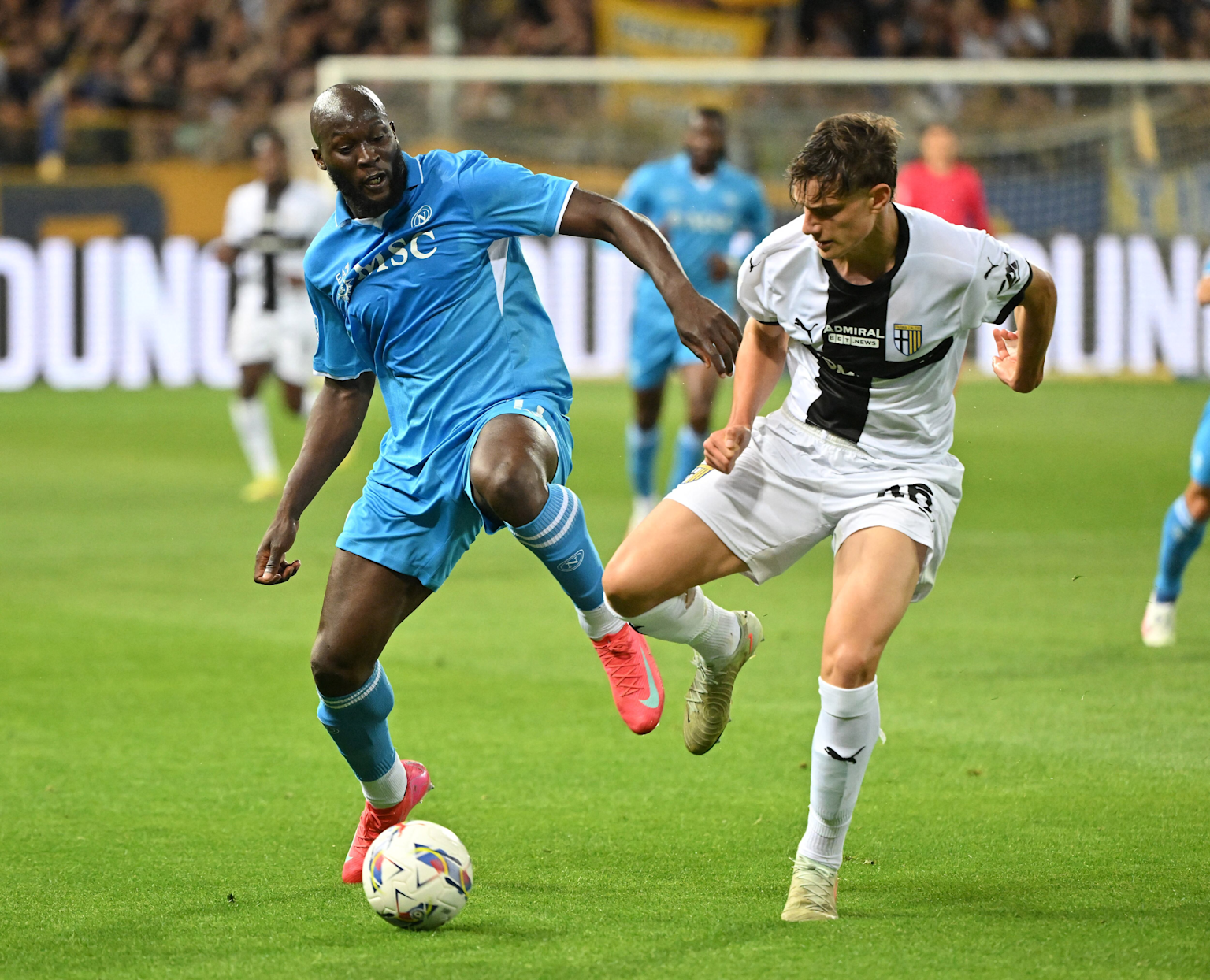 Two soccer players from opposing teams contest the ball during a match on a stadium field