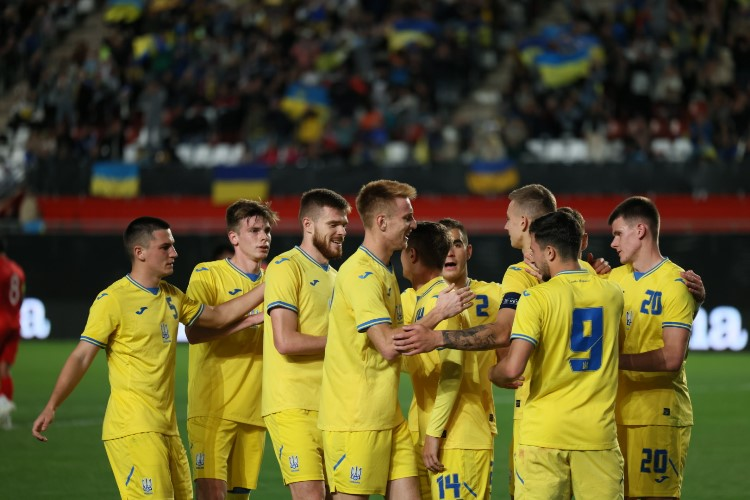 Ukrainian U-21 football players celebrating during a friendly match against Morocco U-23 with fans waving national flags in the stadium