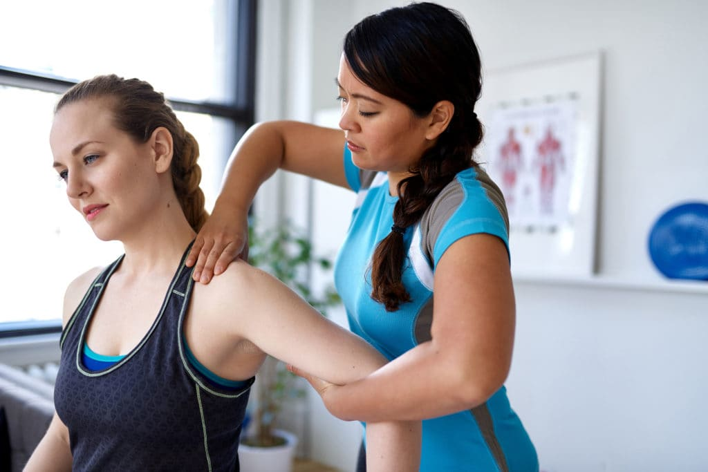 A sports medicine professional assesses shoulder mobility of a female athlete in a clinical setting