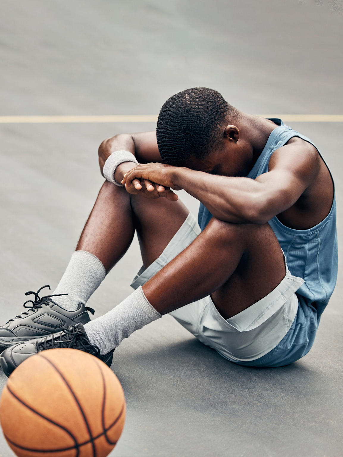 A young basketball player sitting on the court showing signs of exhaustion and burnout in youth sports