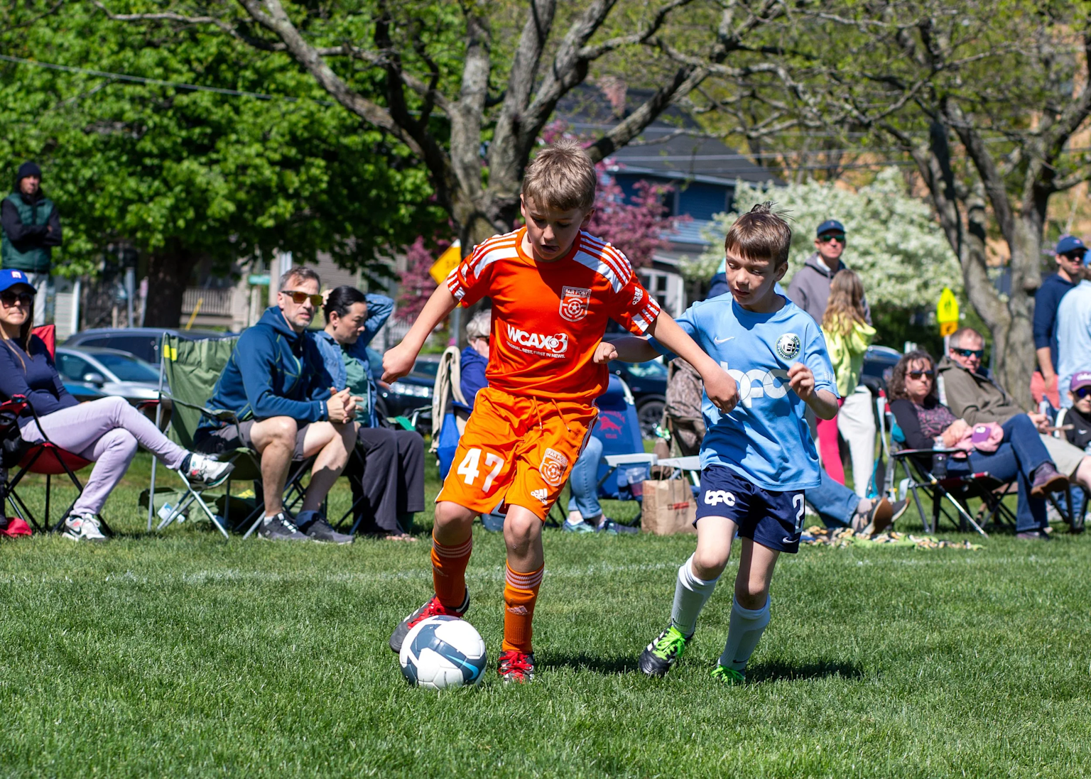 Youth soccer players competing on the field with parents and spectators providing sideline support during a community match