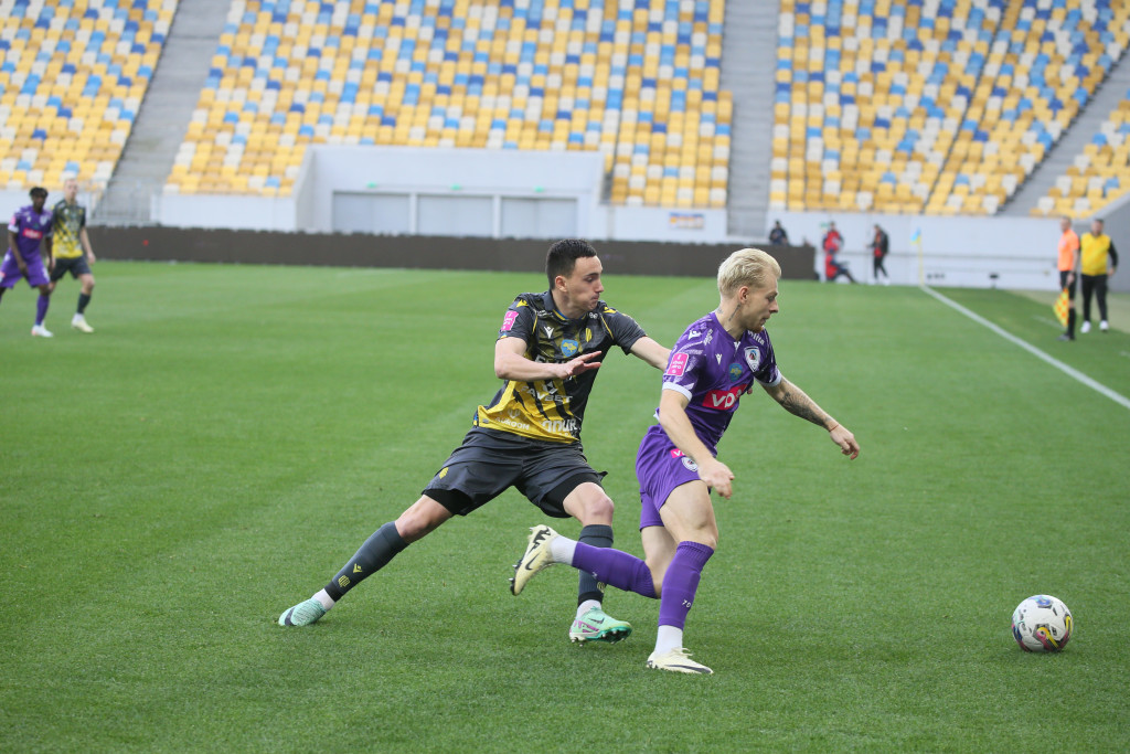 Two football players competing for the ball during a Ukrainian Premier League match inside a stadium with yellow and blue seats