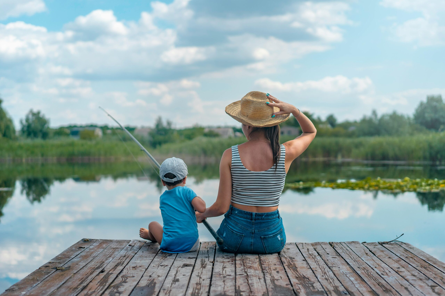 A woman and child fishing together on a quiet lakeside dock, embodying family outdoor relaxation and fishing activities