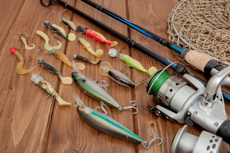 Fishing rods, reels, and a variety of lures displayed on a wooden surface, showcasing fishing equipment