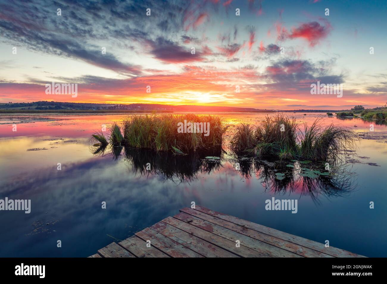 Sunset over a peaceful lake with a wooden dock and grassy islets, ideal for fishing and relaxation