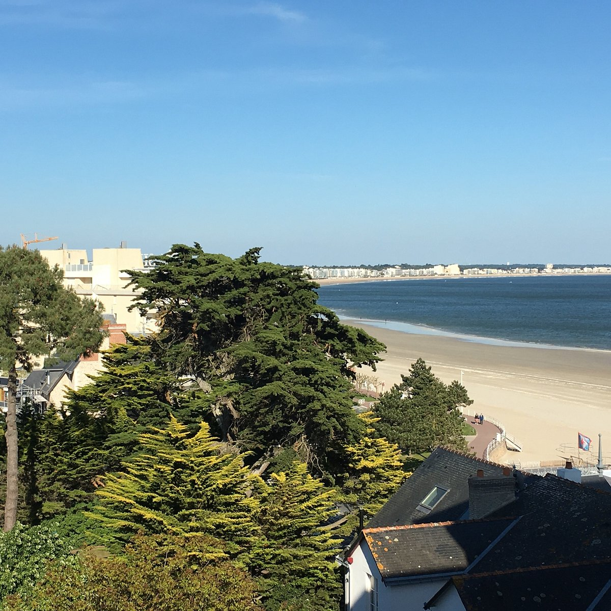 View of the beach and esplanade area in La Baule, France, with trees and buildings in the foreground under a clear sky