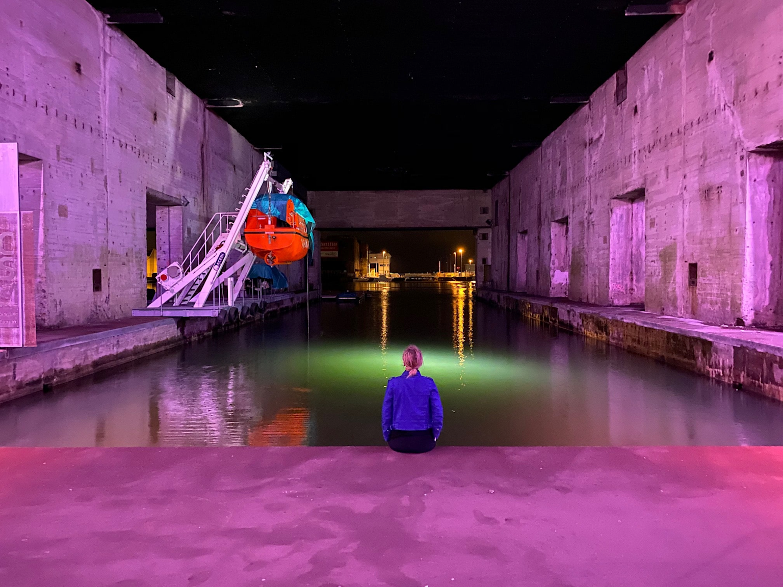 Person sitting inside the illuminated and colorfully lit Base sous-marine of Saint-Nazaire, showcasing a vibrant video mapping or light installation