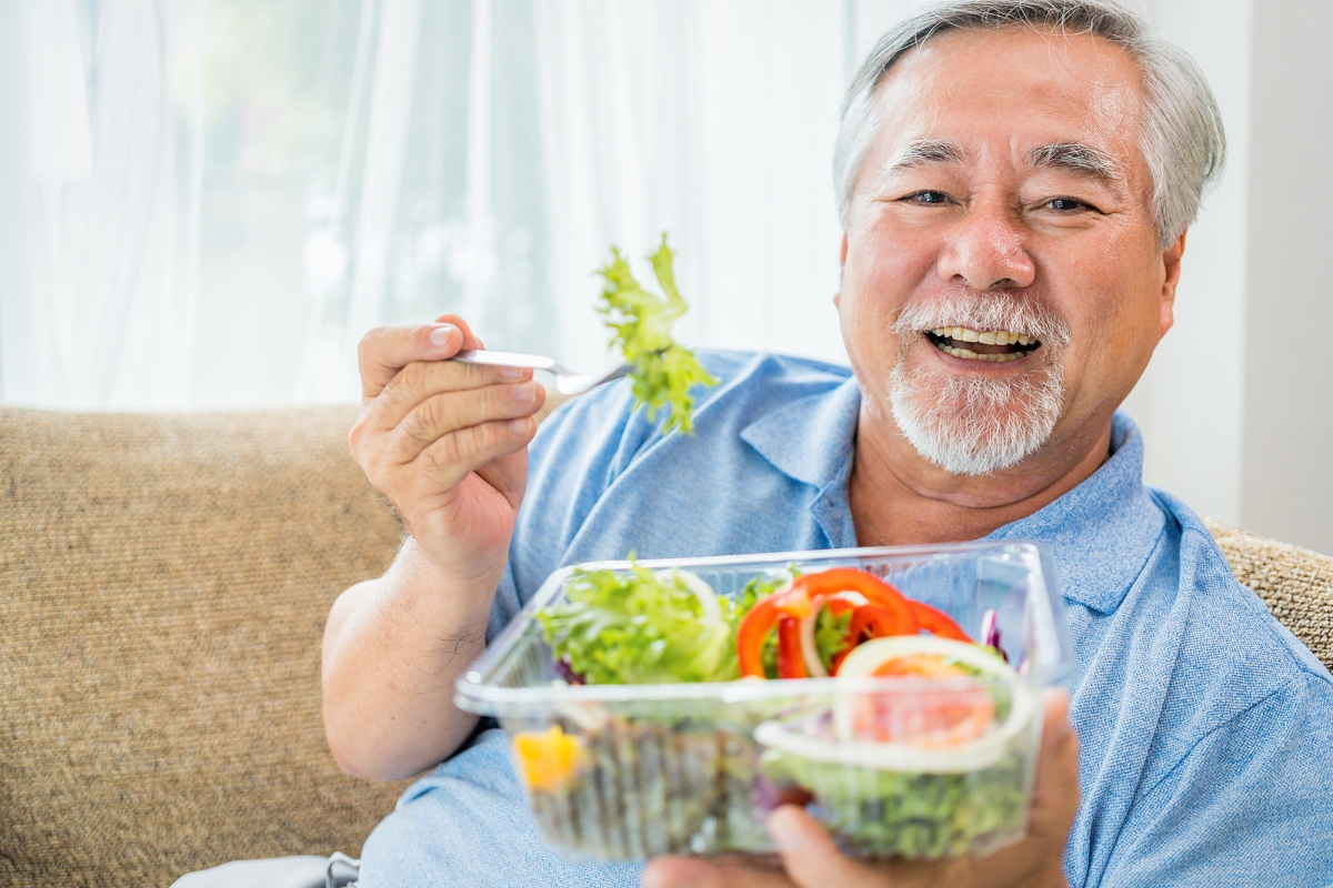 Smiling elderly man eating a fresh vegetable salad at home, illustrating healthy eating habits for seniors