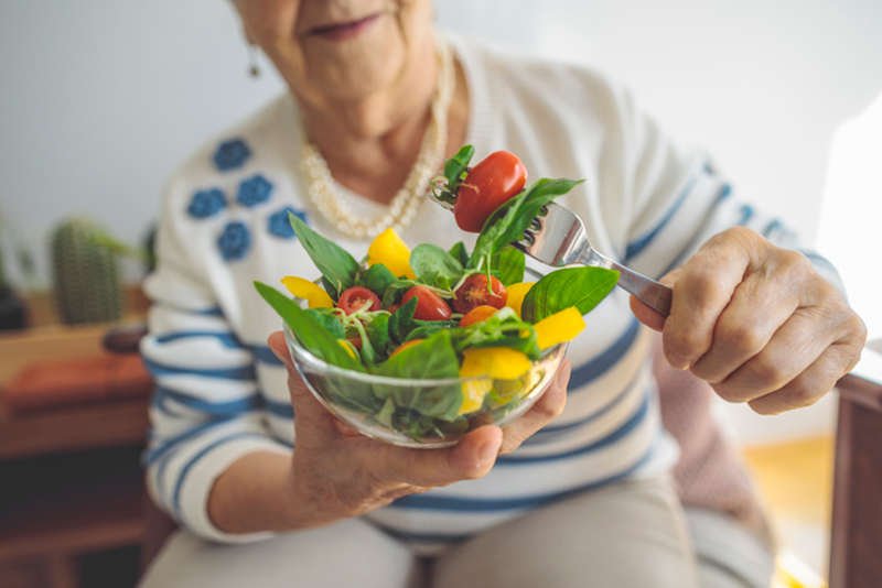 Elderly woman enjoying a bowl of fresh vegetables to support healthy aging and microbiome health