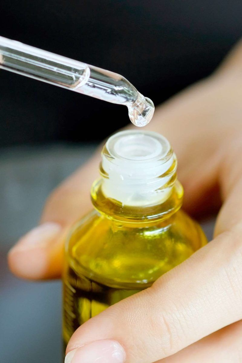 Dropper dispensing essential oil from a yellow bottle, representing natural topical treatment for nail fungus