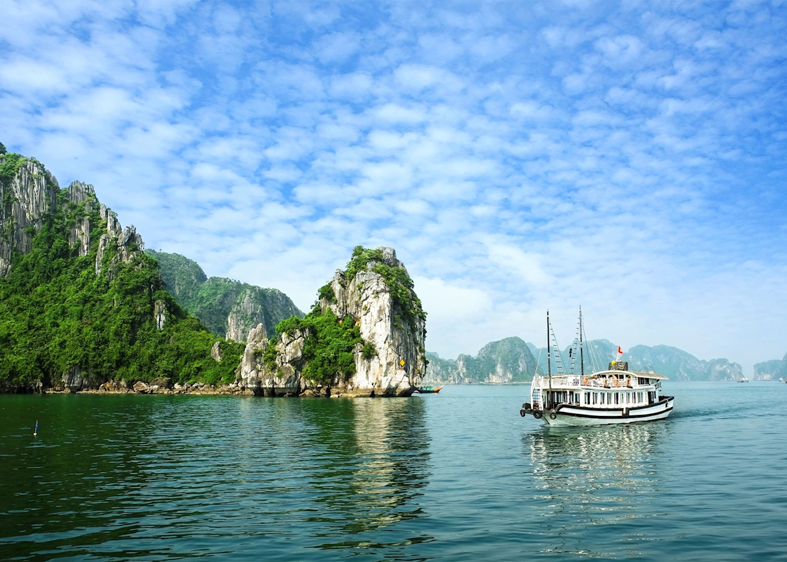 Scenic view of Halong Bay with limestone islands and a boat on calm waters under a blue sky
