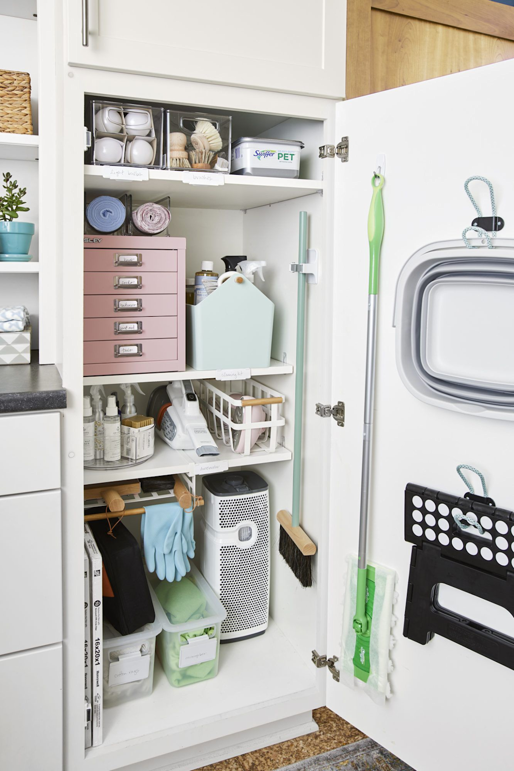 Neatly organized cleaning supplies and tools in a home closet with labeled storage containers, demonstrating effective storage solutions for household cleaning equipment