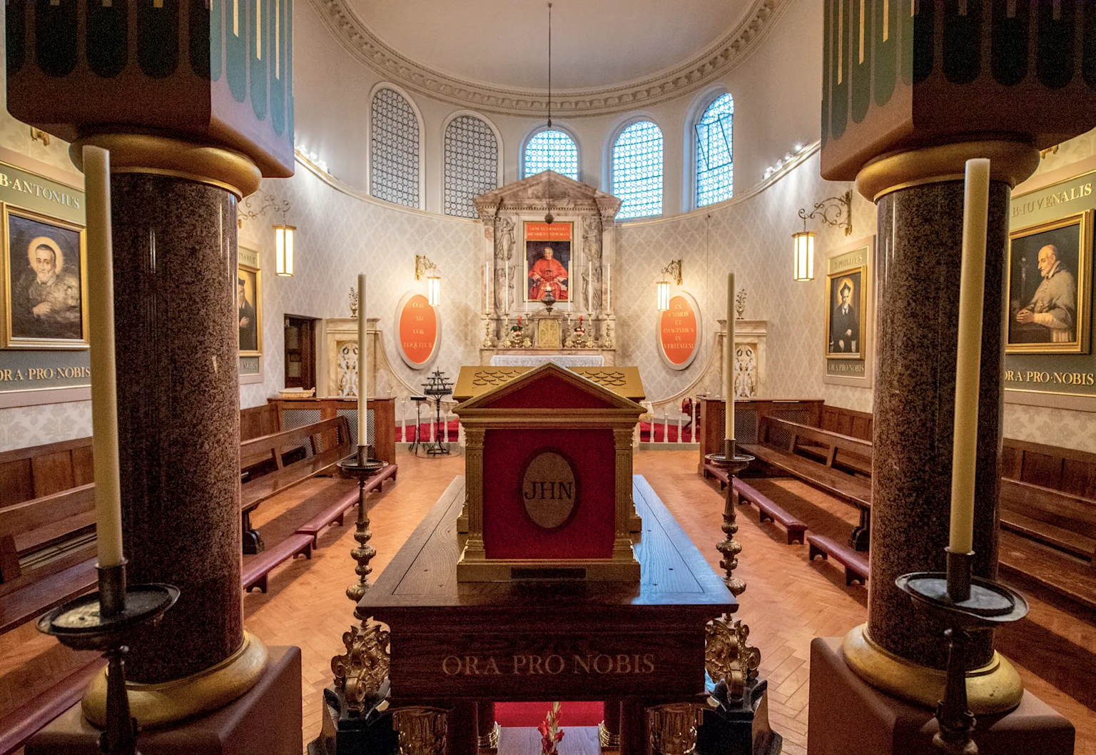 The interior of Newman Chapel in Birmingham Oratory featuring the altar, religious portraits, and Latin inscriptions