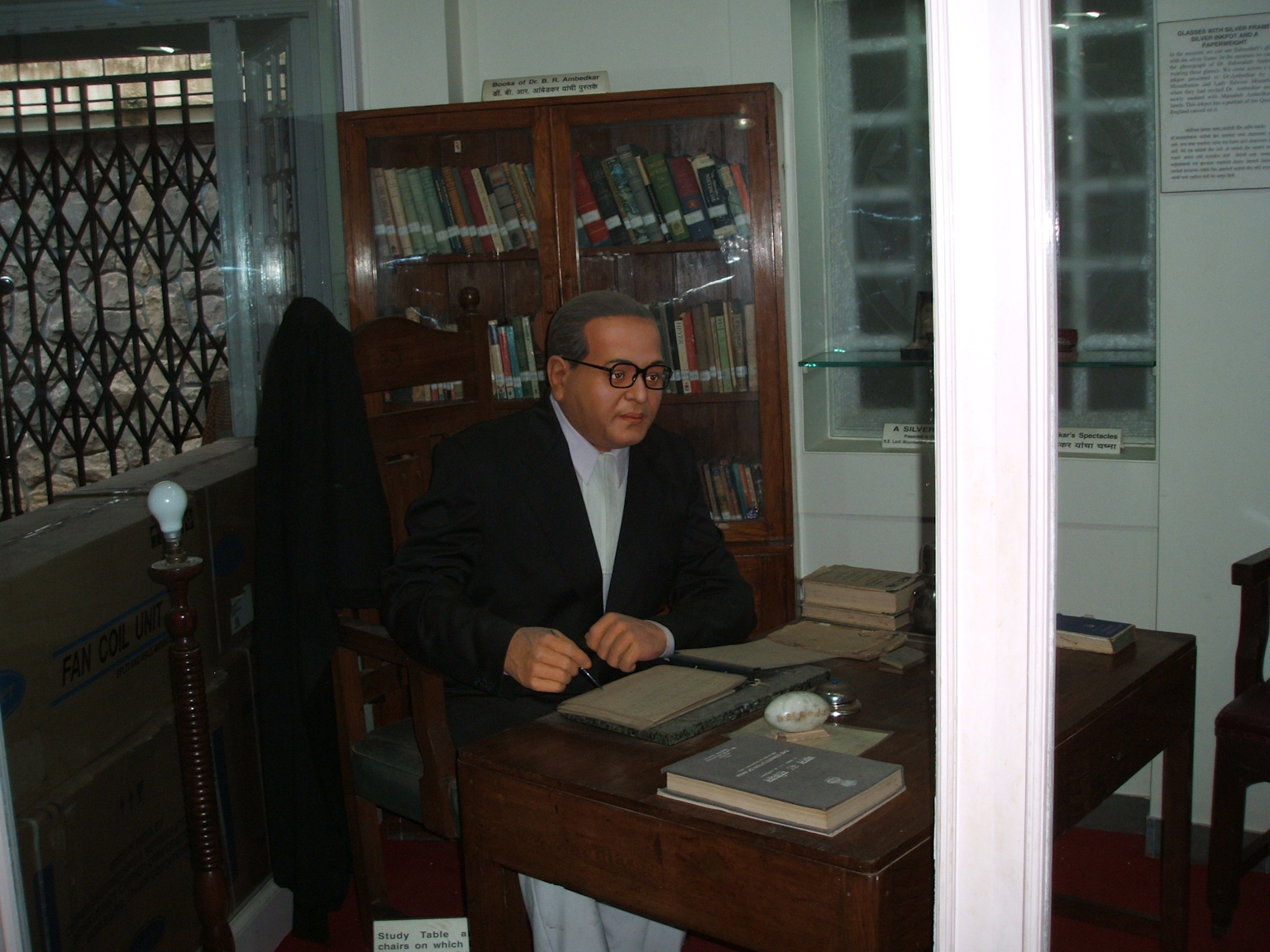 A wax statue of Dr. B. R. Ambedkar at his study table surrounded by his personal library, highlighting his intellectual environment and reading habits