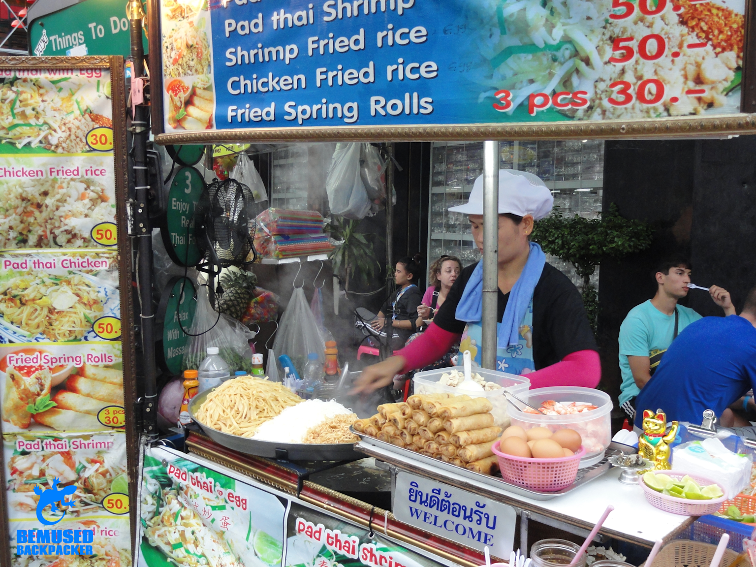 A vibrant street food stall in Southeast Asia offering budget-friendly dishes like Pad Thai and spring rolls with visible prices, showcasing affordable local cuisine