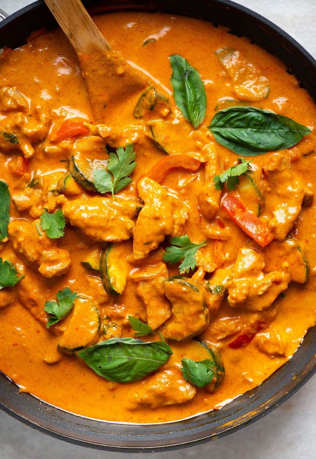 Close-up of creamy chicken Thai red curry garnished with fresh basil and cilantro in a bowl with a wooden spoon