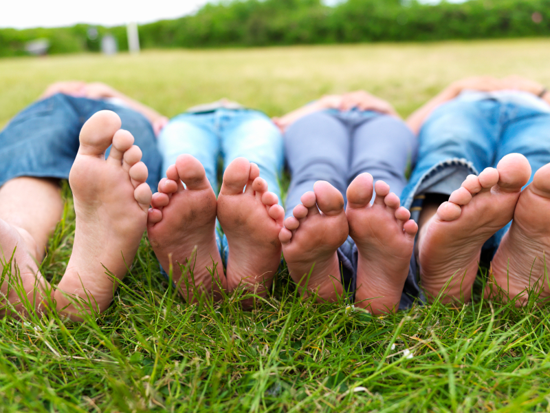 A family lying on grass showing their bare feet prominently, illustrating family foot care and hygiene
