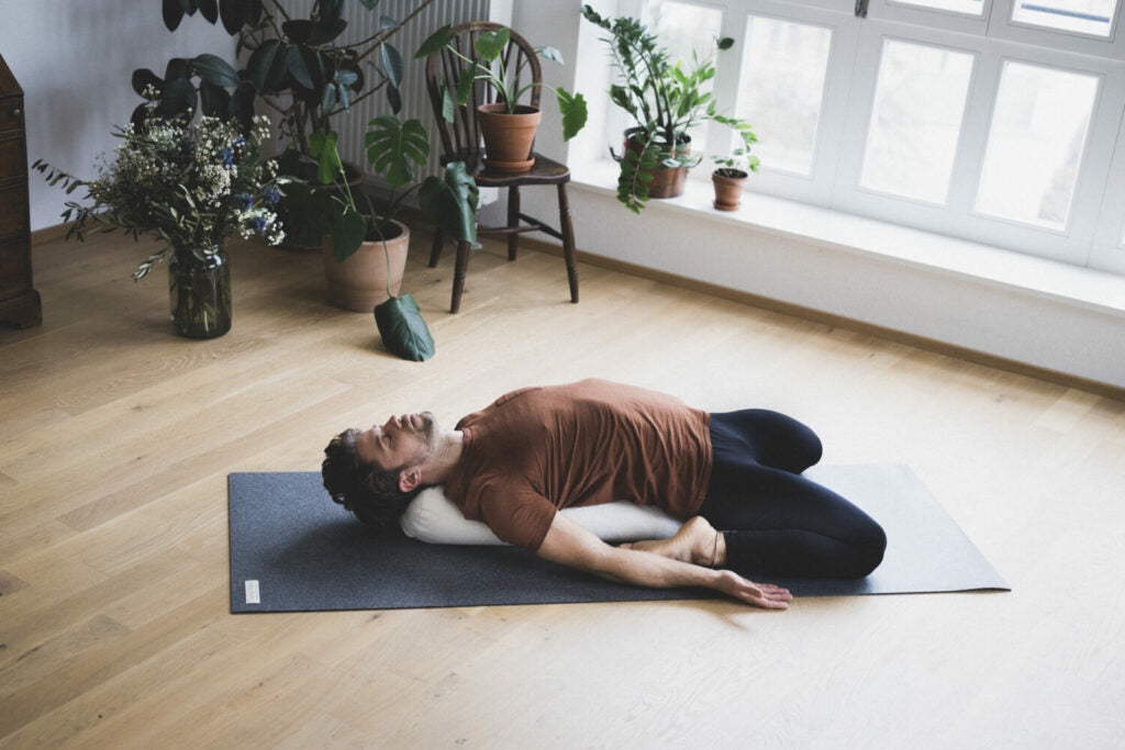 Man practicing yin yoga with a bolster for relaxation in a peaceful indoor setting