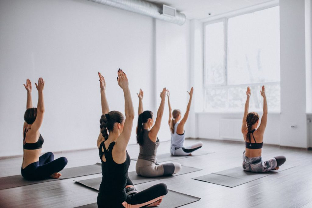 A realistic photo of a beginner Hatha yoga class performing a seated pose with arms raised