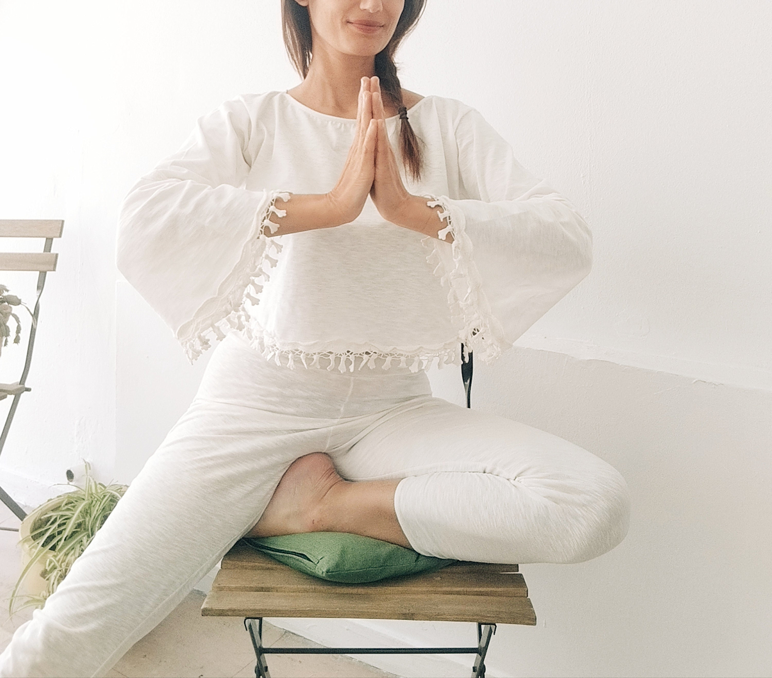 A woman in white clothing practicing a meditative pose seated on a chair