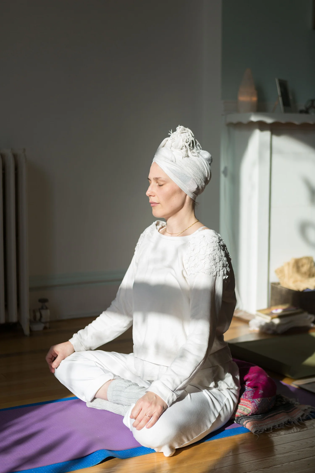 A woman meditating in a white outfit and turban during a Kundalini yoga session indoors