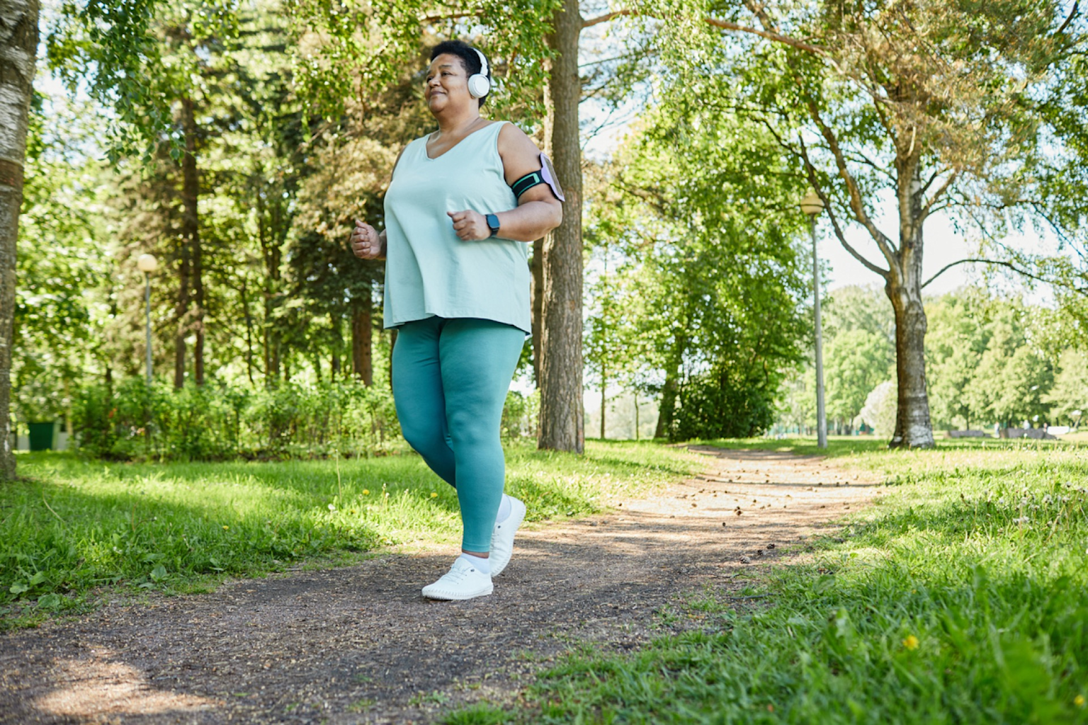 Person walking briskly outdoors on a trail in a green park, suitable for interval walking training to lose weight.