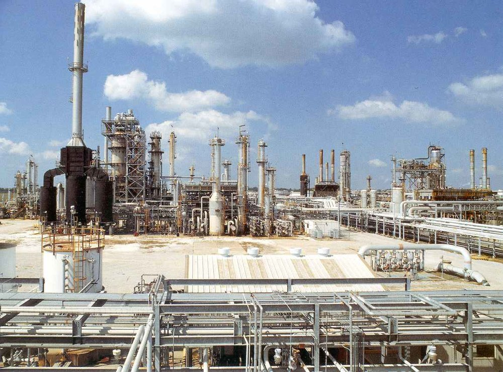 A large petrochemical refinery complex with numerous towers and pipelines under a partly cloudy sky