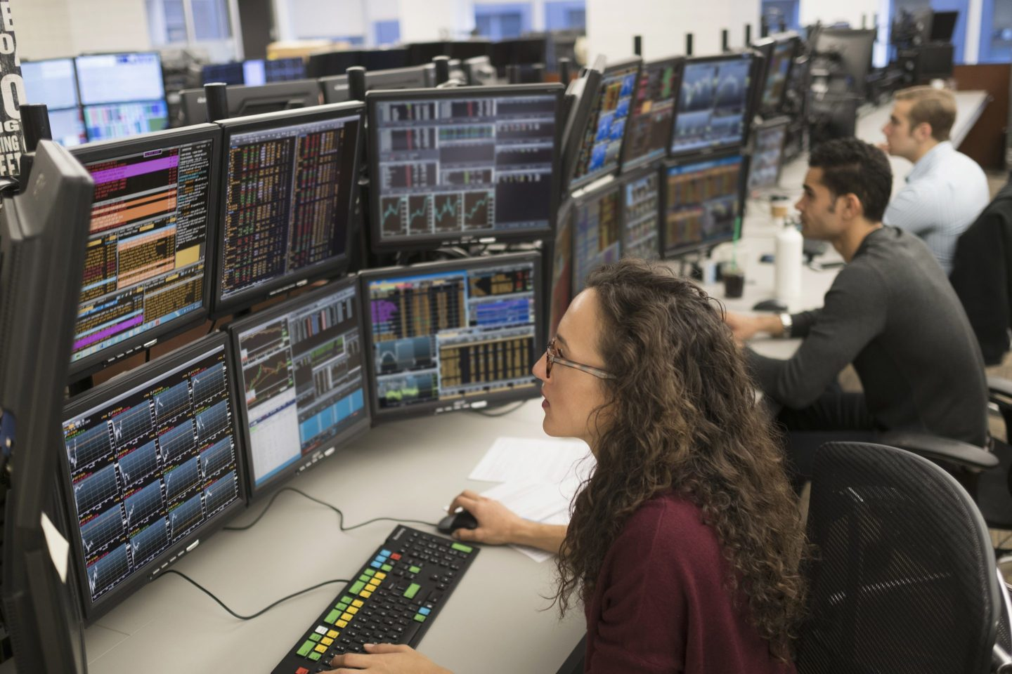 Financial analysts working on a trading floor with multiple monitors displaying real-time market data and analysis tools
