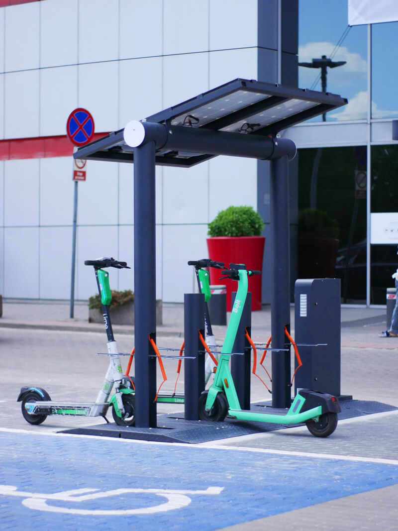 Modern electric scooter charging station with solar panels and parked e-scooters from Lime and Bolt brands