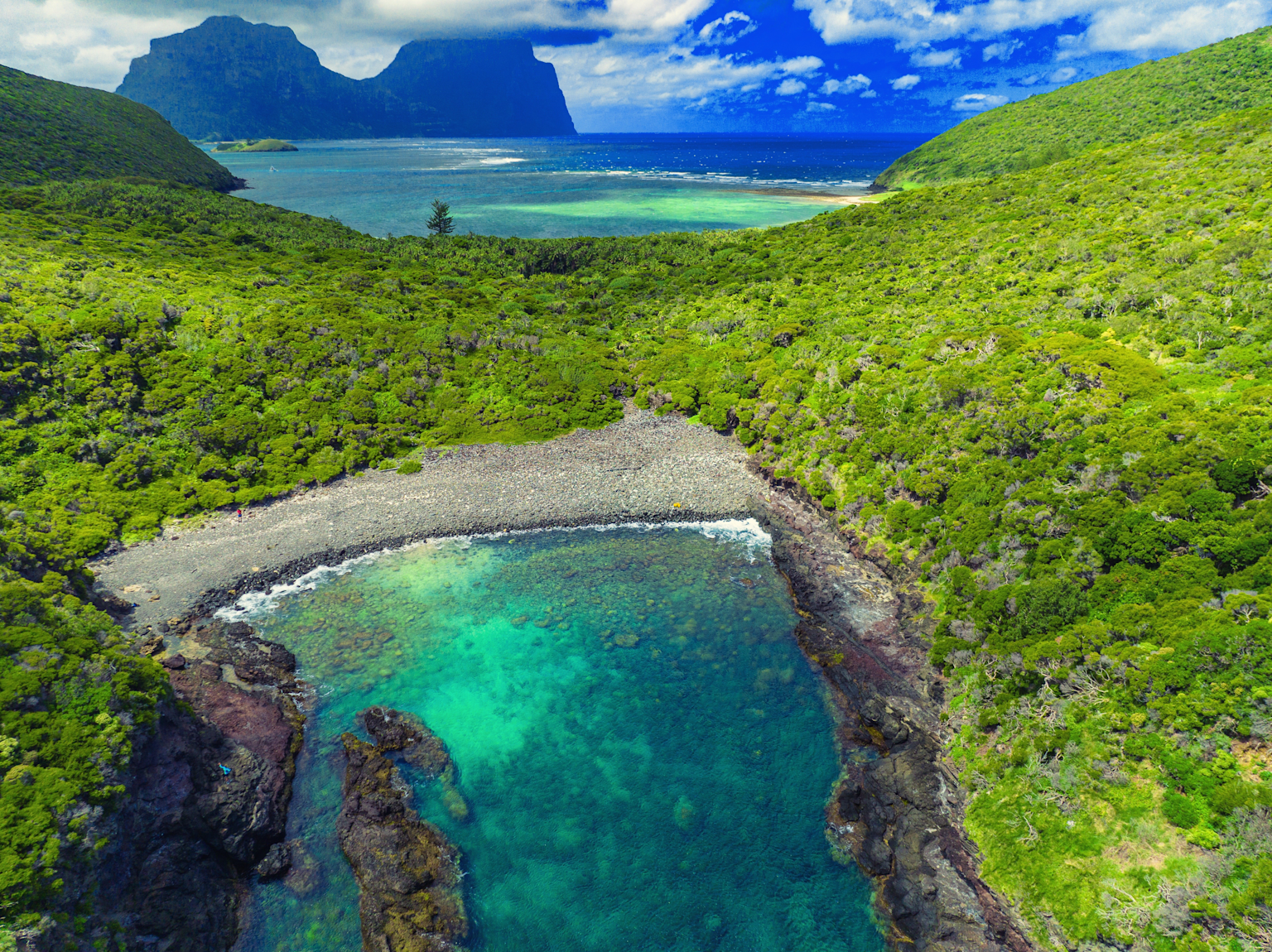Aerial view of Lord Howe Island's vibrant green hills and crystal-clear lagoon with Mount Gower in the distance
